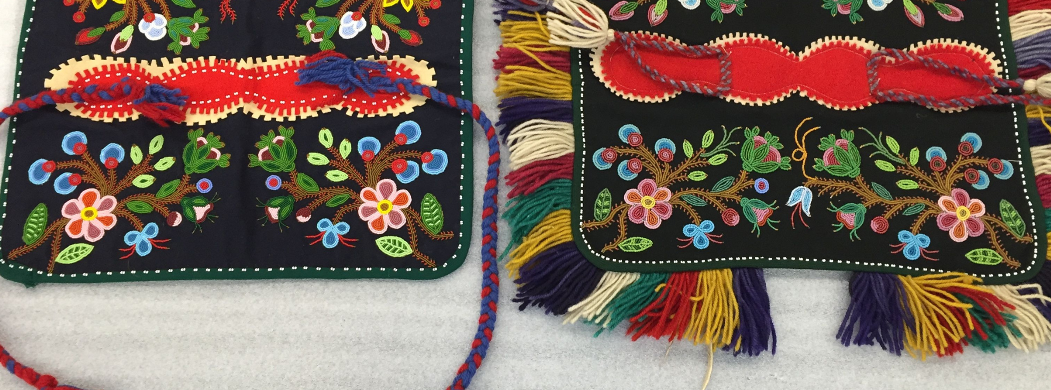 Two intricately beaded square dog blankets. The one on the right has a colourful fringe around the edges, and the one of the left does not, instead having two longer braids as ties. The pattern on the body of each piece is nearly identical.