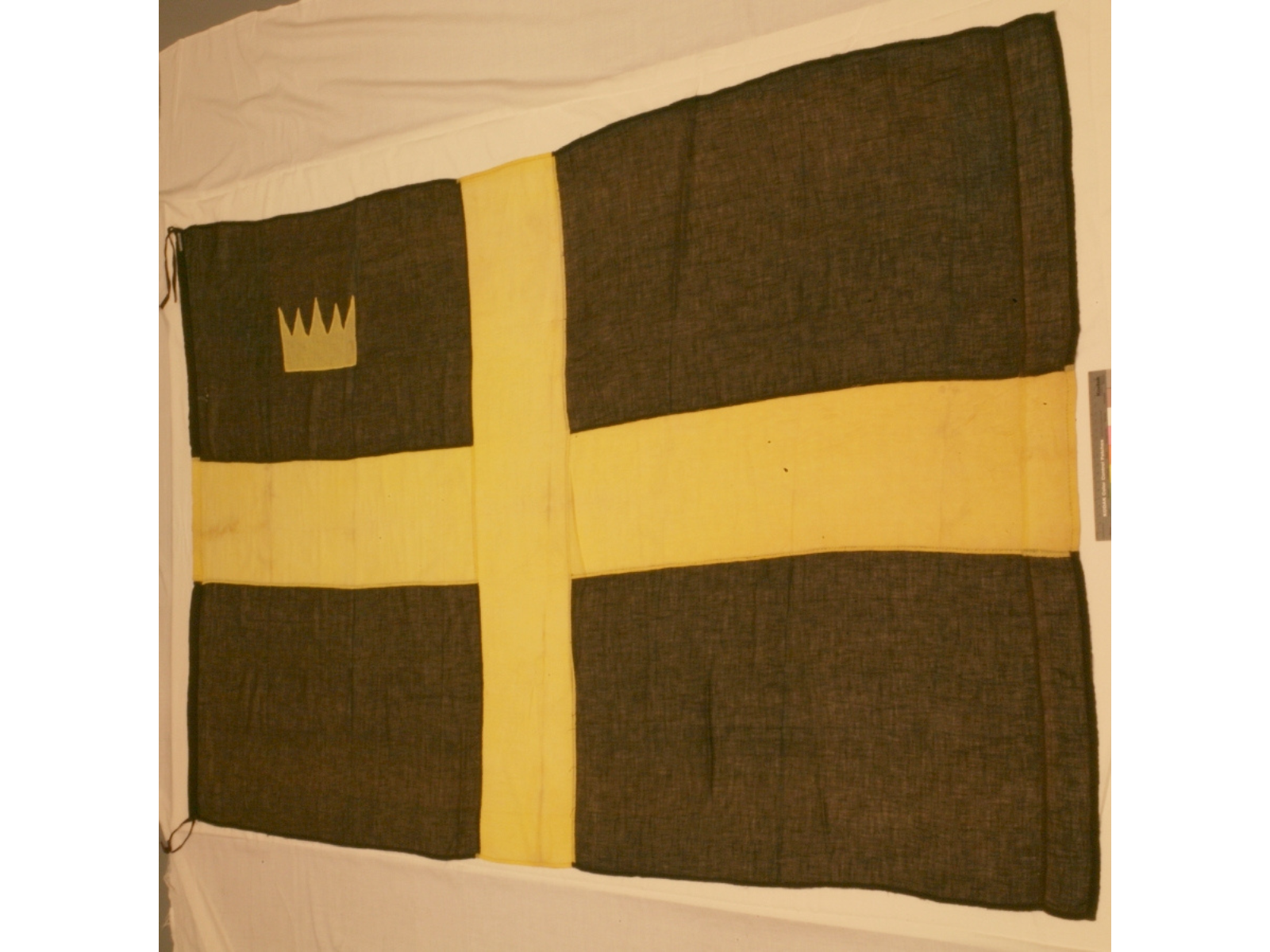 A large flag in brown material with a yellow cross through it. In the upper left quadrant is a yellow crown.