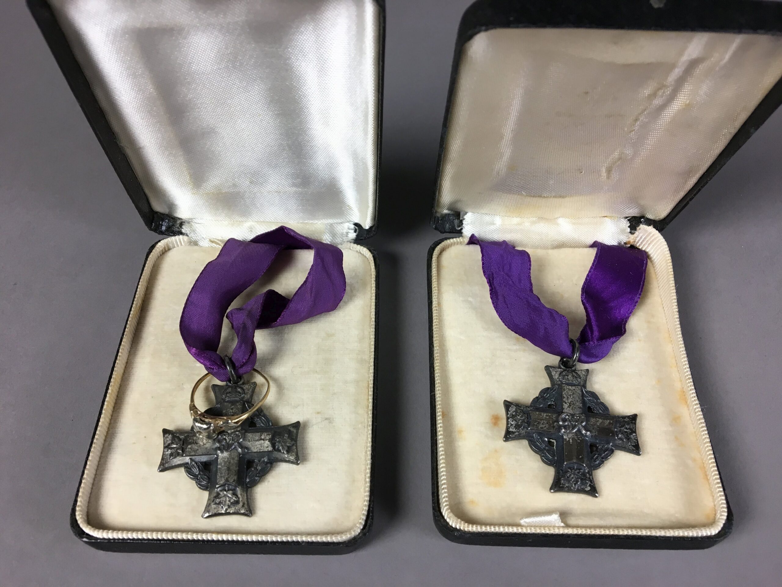 Two Memorial Cross medals on purple ribbons each in a medal box. The medal on the left has an engagement ring fastened to the ribbon.