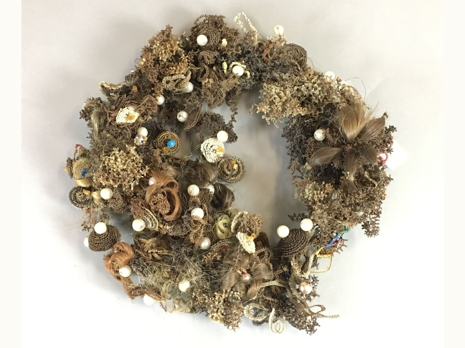A haighly decorative wreath woven of varying shades of brown and blonde human hair, with occasional accent beads.