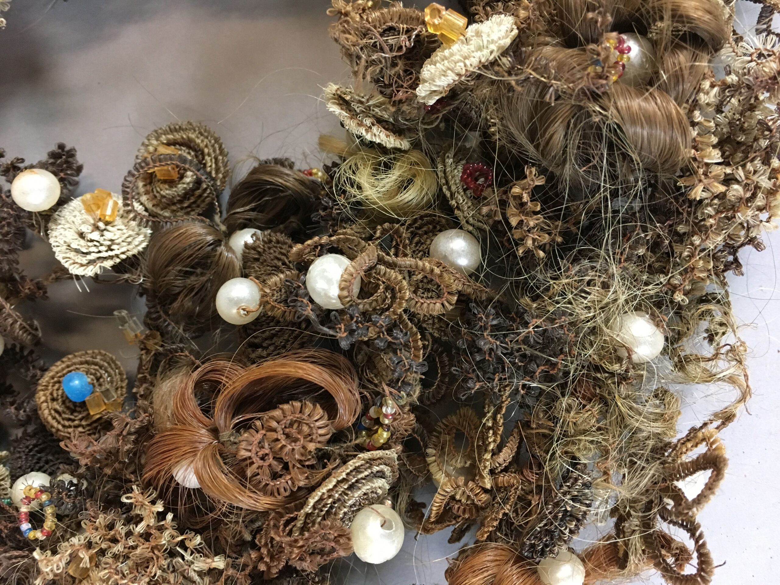 Close up on a portion of a highly decorative wreath woven of varying shades of brown and blonde human hair, with occasional accent beads.