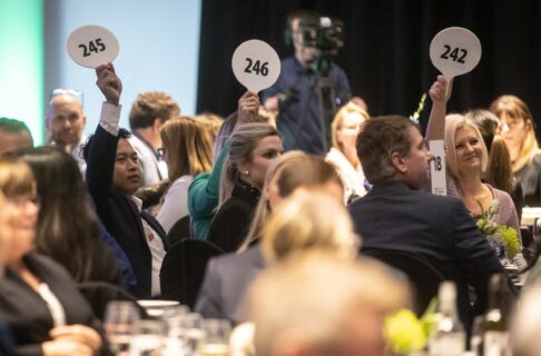 Looking into the audience at a Tribute Gala, as three attendees raise paddles during the auction.