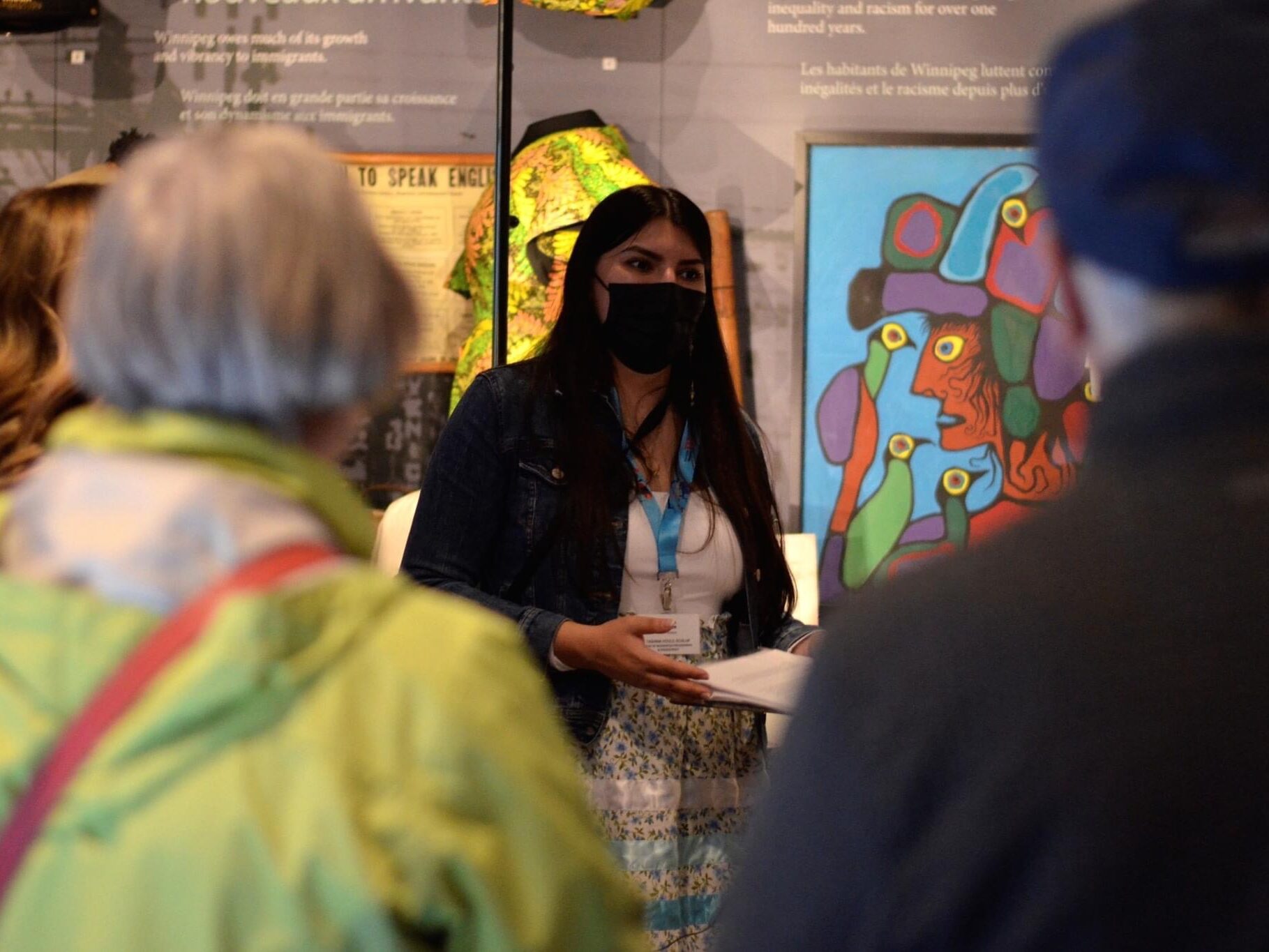 A masked female guide speaks to a group of adults.