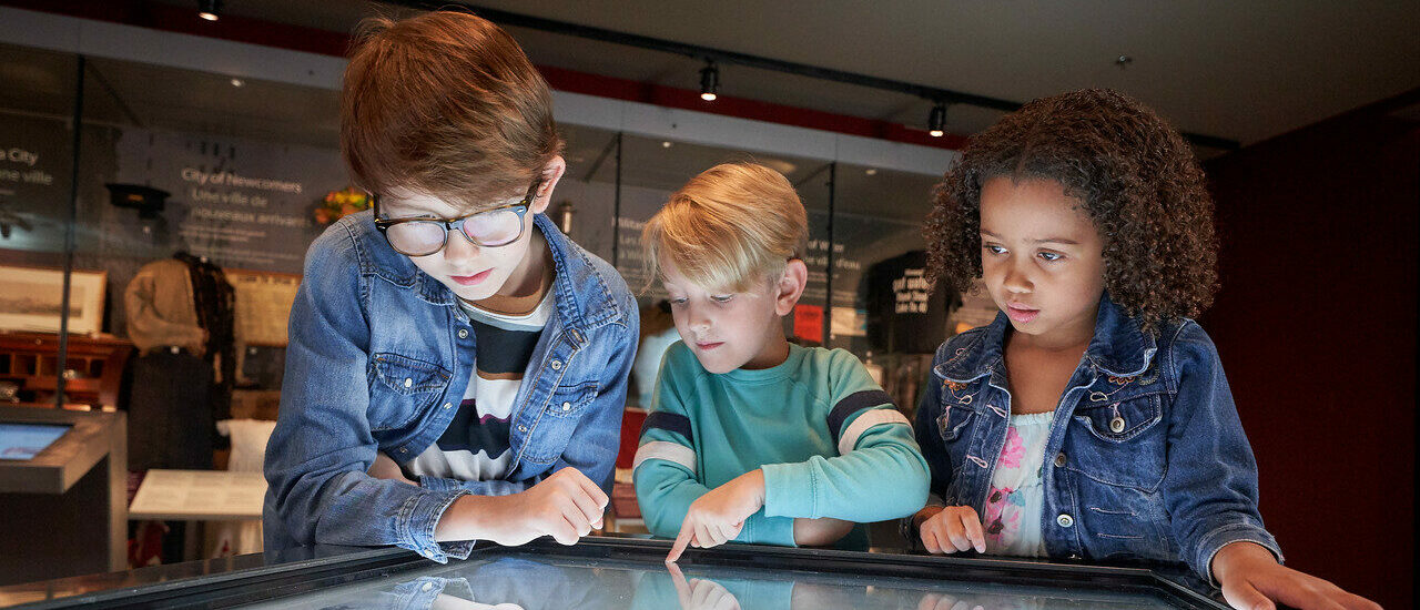 Three children interact with a exhibition digital screen in a museum gallery.