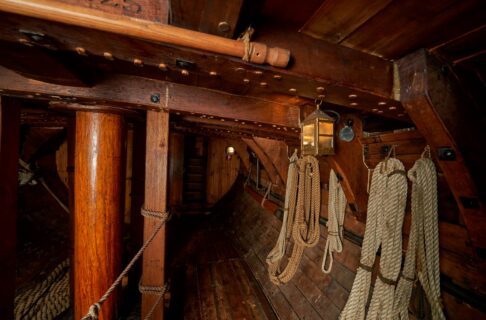 The wooden hold of the Nonsuch. Coiled ropes hand on the curved walls to the right.