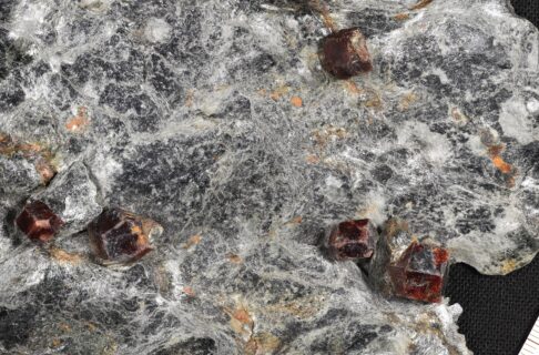 A close-up view of the surface of a rock shows beautiful red-brown crystals lying on a glossy grey surface.