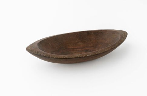 A dark brown, oval dish carved from wood with zig-zag and triangular carvings along the edge.