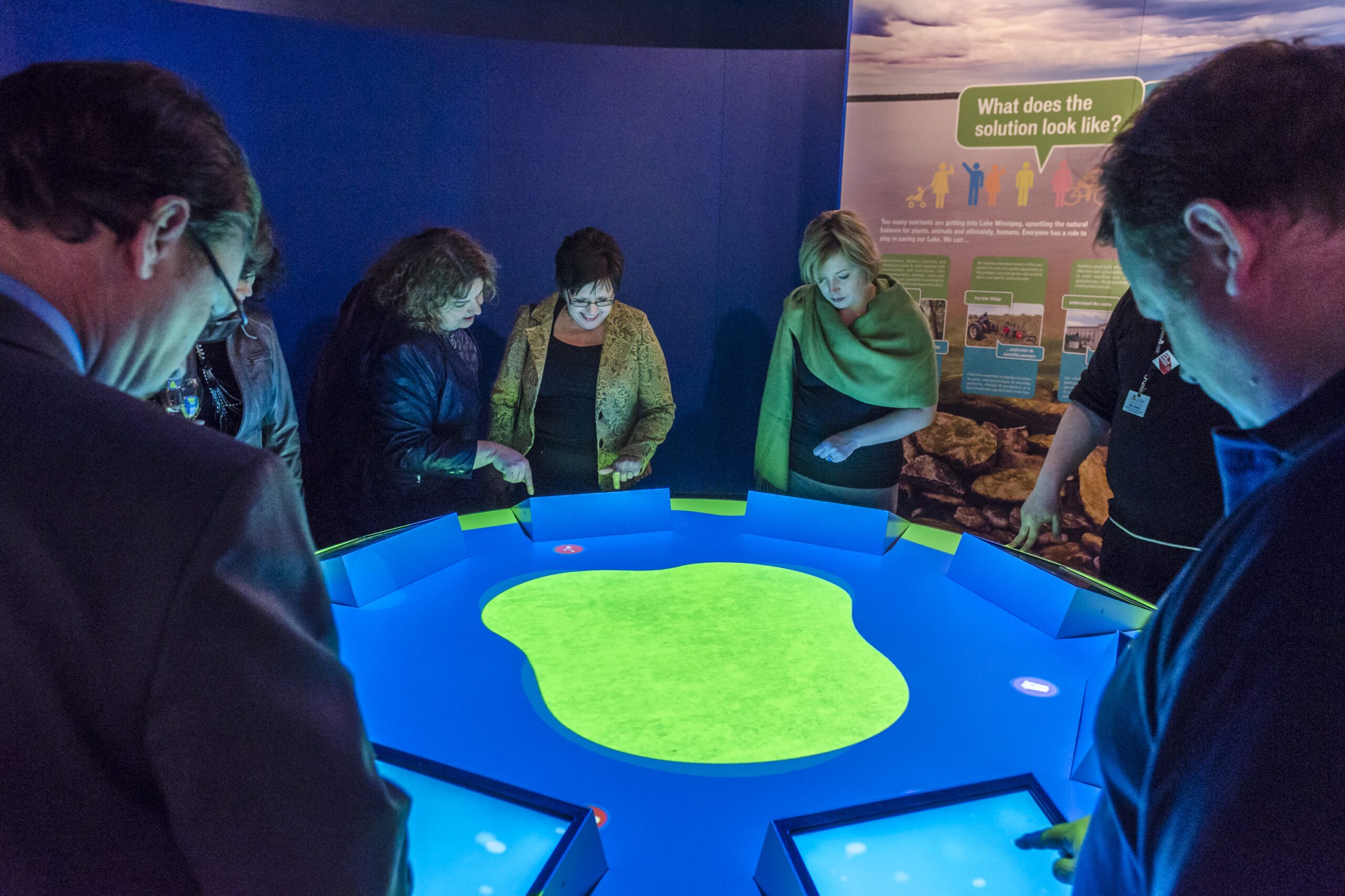 People in business attire engaging with the Lake Winnipeg Shared Solutions simulator in the Science Gallery.