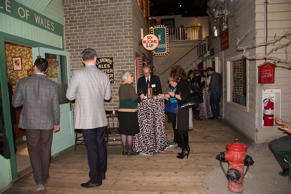 People in business attire walking around and standing at cocktail tables in the Winnipeg 1920 Cityscape.