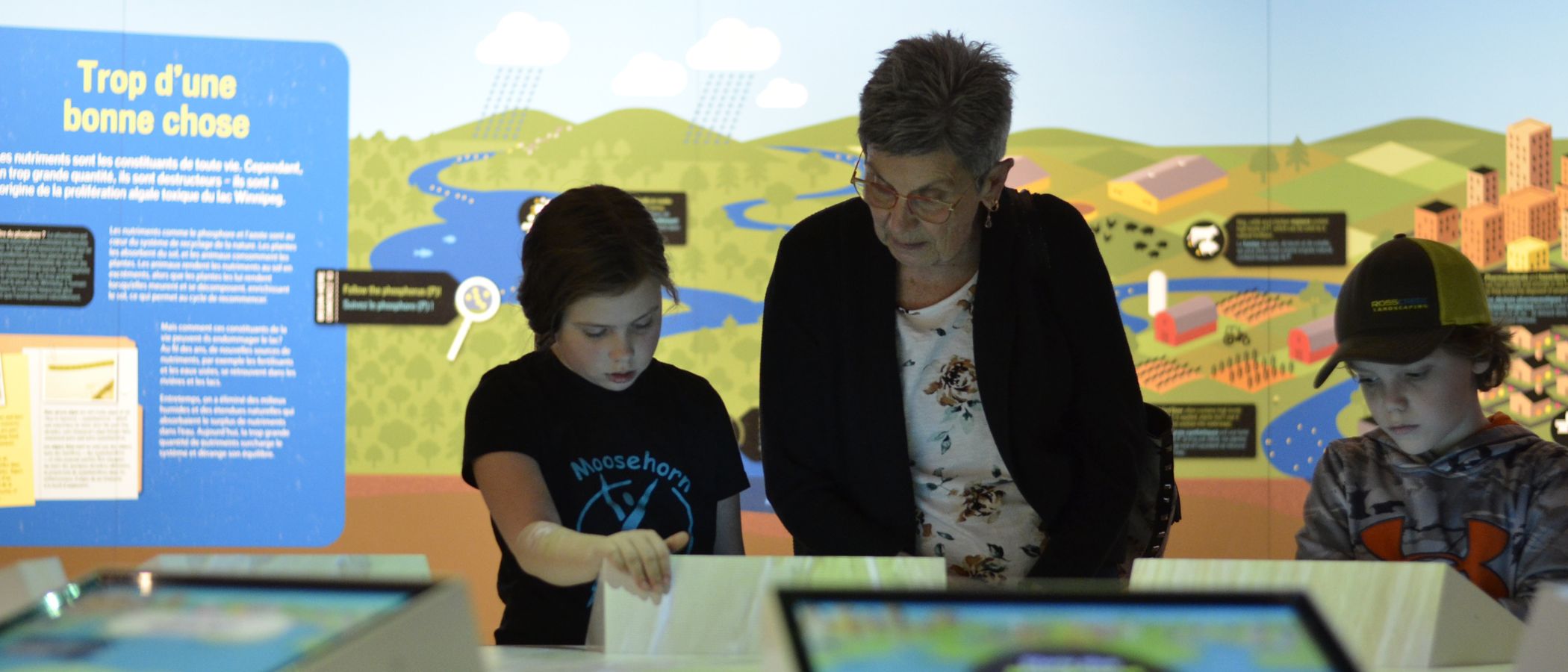An adult and two children interact with digital displays and projection that show the changing environment of Lake Winnipeg.
