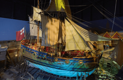 Photograph of a large wooden ship (the Nonsuch) with her sails out “in dock” in the Nosuch Gallery of the Manitoba Museum.
