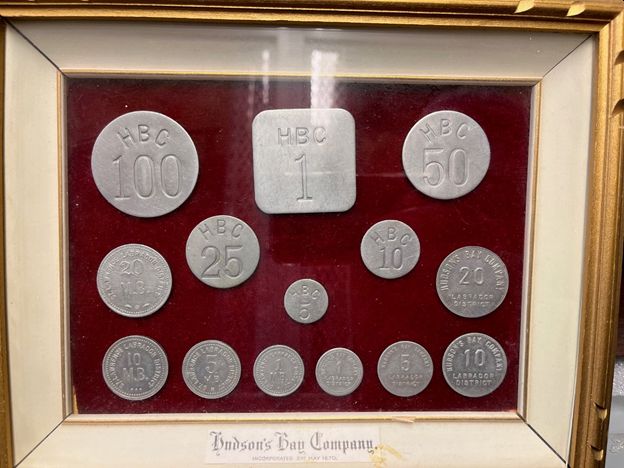 A set of aluminum trade tokens marked HBC or Hudson's Bay Company in a frame on red velvet backing.