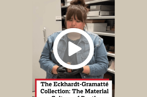 A screenshot of a video, an individual standing in a collections space in front of full shelves looking down at an artifact they're holding. There's a play button over the screenshot and overlaid text reads, "The Eckhardt-Gramatté Collection: The Material Culture of Death".
