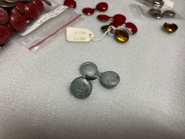 Two grey (zinc) bale seals in the front and red enamel-coated ones in the back, all featuring HBC coat of arms.