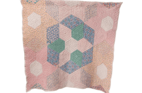 A quilt stitched of pastel pink, orange, and cream fabric with an accent portion in the middle in blues and greens.