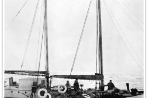 Black and white photograph looking onto the deck of a smaller ship with two masts, with several people on board.