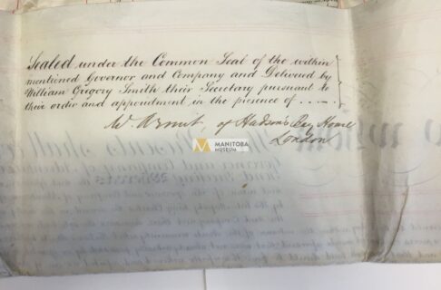 Photograph of the basckside of a folded piece of paper with formal cursive writing and signatures on it, starting, “Sealed under the Common Seal of the within mentioned Governor and Company”.