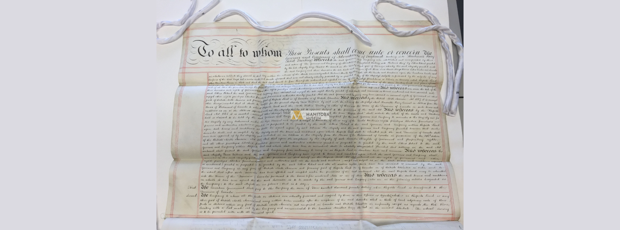 Photograph of a large sheet of paper filled with very formal cursive writing. The writing starts off, “To all whom these presents shall come unto, or concern, the Governor and Company of Adventurers of England,”.