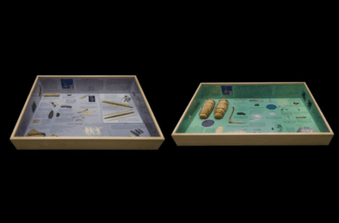 Two display cases. Left: Looking into a blue display case shadow box with photographs and illustrations of artifacts as well as descriptive text. Right: Looking into a green display case shadow box with photographs and illustrations of artifacts as well as descriptive text.