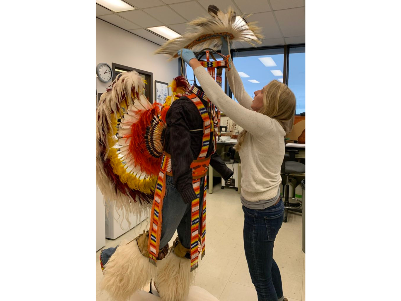 Conservator Carolyn Sirett adjusts the headdress of Pow Wow regalia on a mannequin in the conservation lab.
