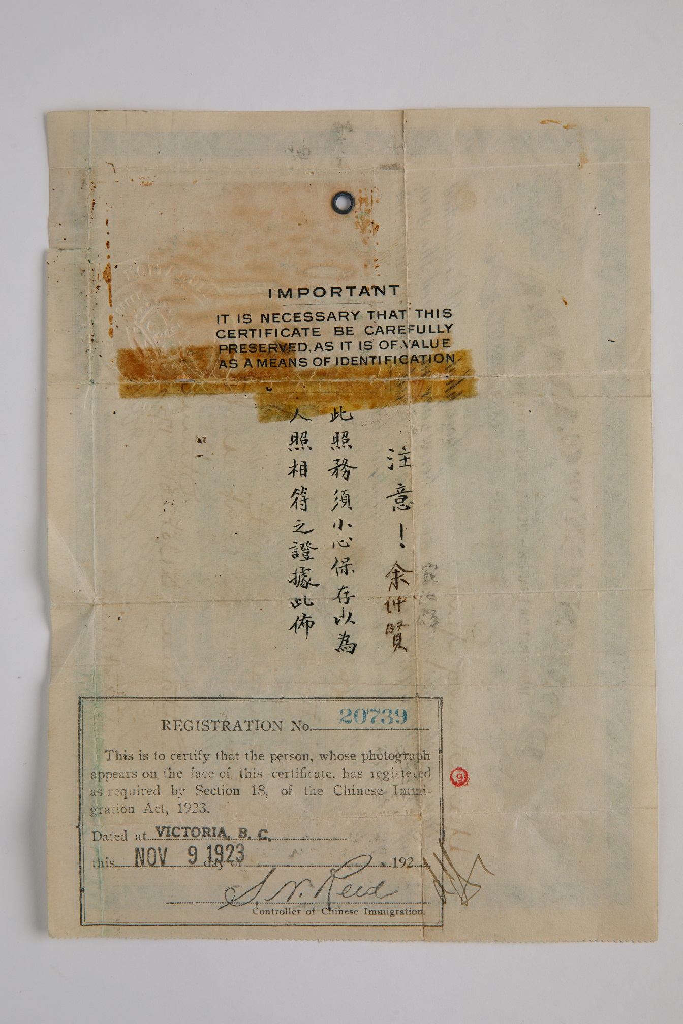Photograph of the backside of a piece of paper. In the centre is stamped, “IMPORTANT / It is necessary that this certificate be carefully preserved as it is of calue as a means of identification”. In the bottom left corner is a registration number and certification stamp, date, and signature.
