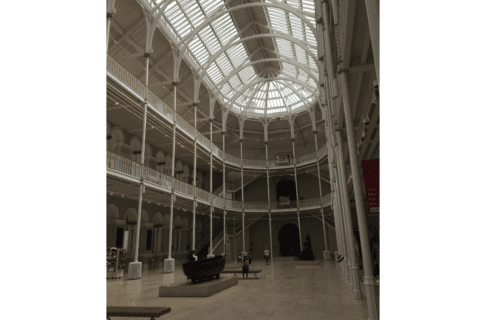 Looking into a large gallery space with a oval domed glass ceiling. Two wrap around balconies show second and third levels to the building.