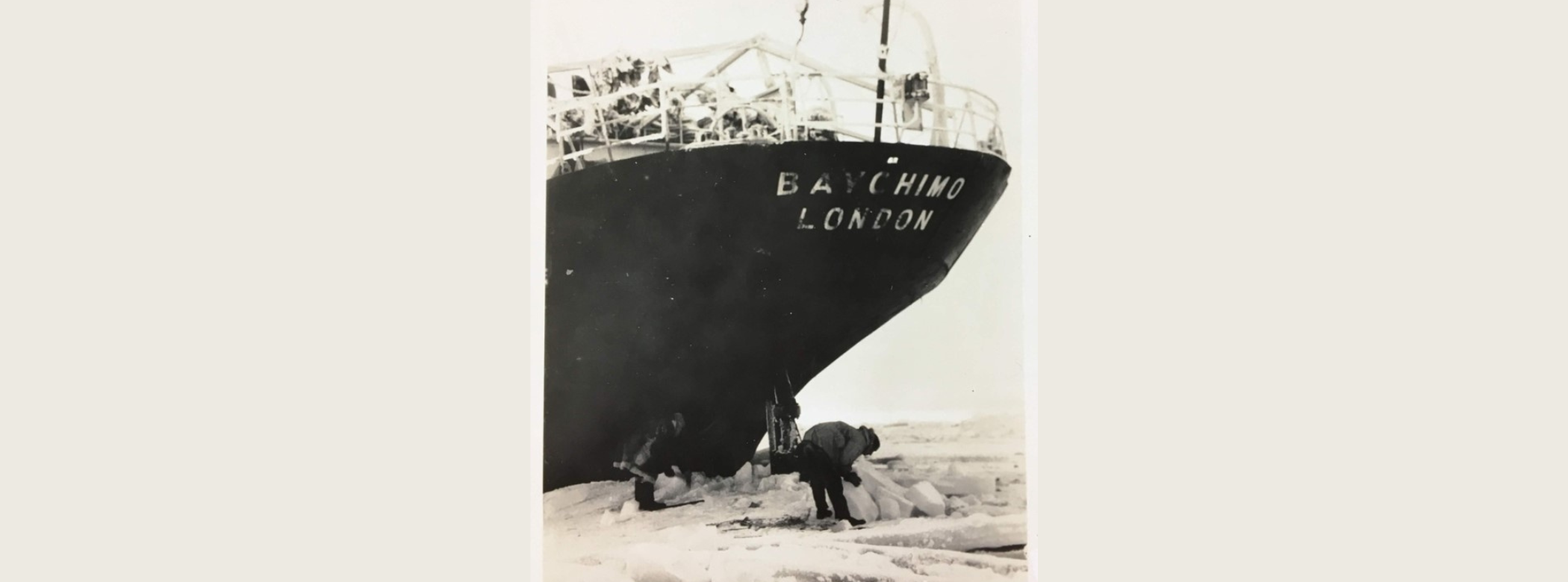 Black and white photograph of two individuals on thick ice below the stern of the ship “BAYCHIMO”.