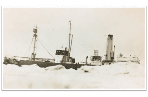 Sephia-toned photograph of a steam ship with ice reaching high up on its sides and at its stern.