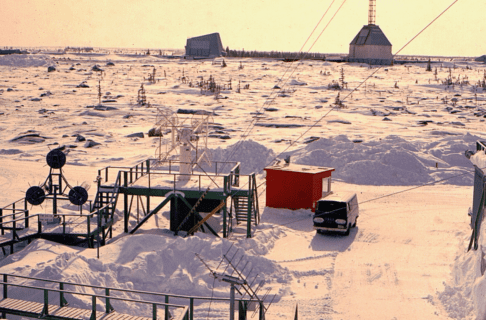 Low viewing platforms and ramps built into a snowy landscape looking towards two larger industrial buildings in the distance.