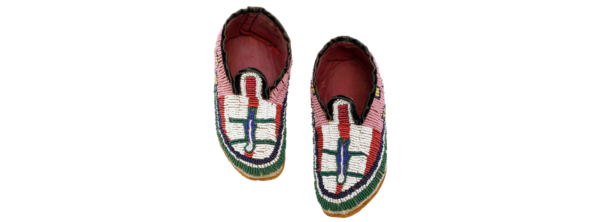 A pair of child’s moccasins with toes pointing down. The insides are lined with pink fabric, and the exterior is covered in brightly coloured glass beads. The beads are pink near the ankle, the vamp has white and red along with a figurative image in the centre, and the edges are lined with rows of blue, white, and green.