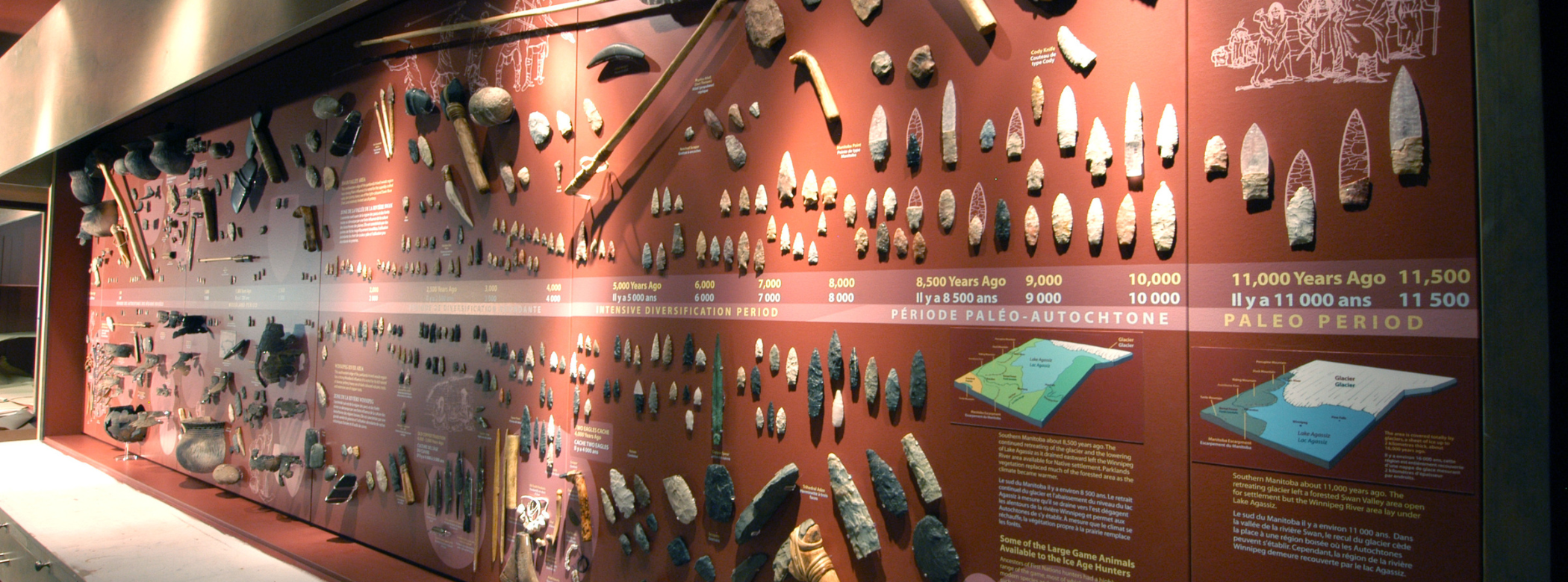Hundreds of archaeological artifacts attached to a gallery wall, including spears, arrowheads, axes, and ceramic sherds.
