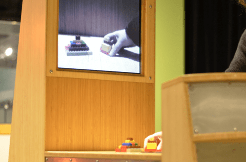 A digital screen reflecting the LEGO figures being moved on the table in front of it by an individual out of frame.