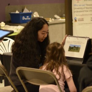 A student researcher going through a study activity with a child in the Explore Science Zone.