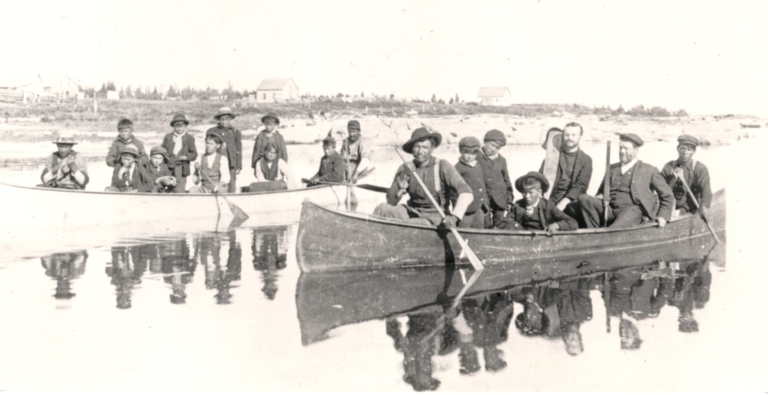 Sepia photograph of two canoes on a body of water, each with several children and adults in it.