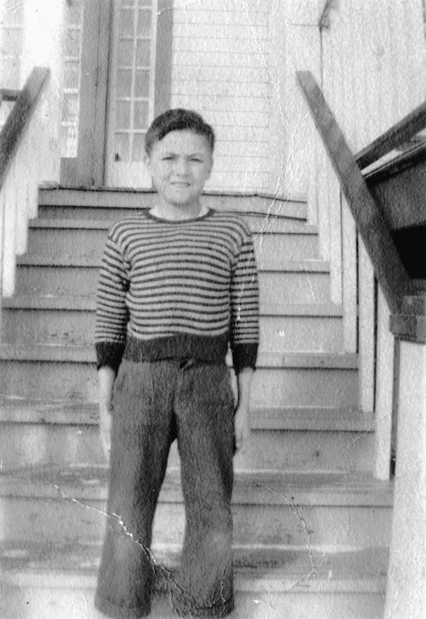 Black and white photograph of a child standing on outdoor stairs leading up to a door.