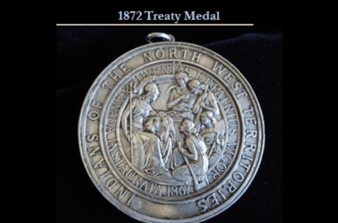 Photograph of a highly decorative circular silver medal portaying a scene with Imperial Britannia, a lion, and Roman maidens clustered together. Text around the edge of the medal reads, “Indians of the North West Territories / Juventas et Patrius Vigor / Canada Instaurata 1867”. Text has been overlaid at the top of the image, reading, “1872 Treaty Medal”.