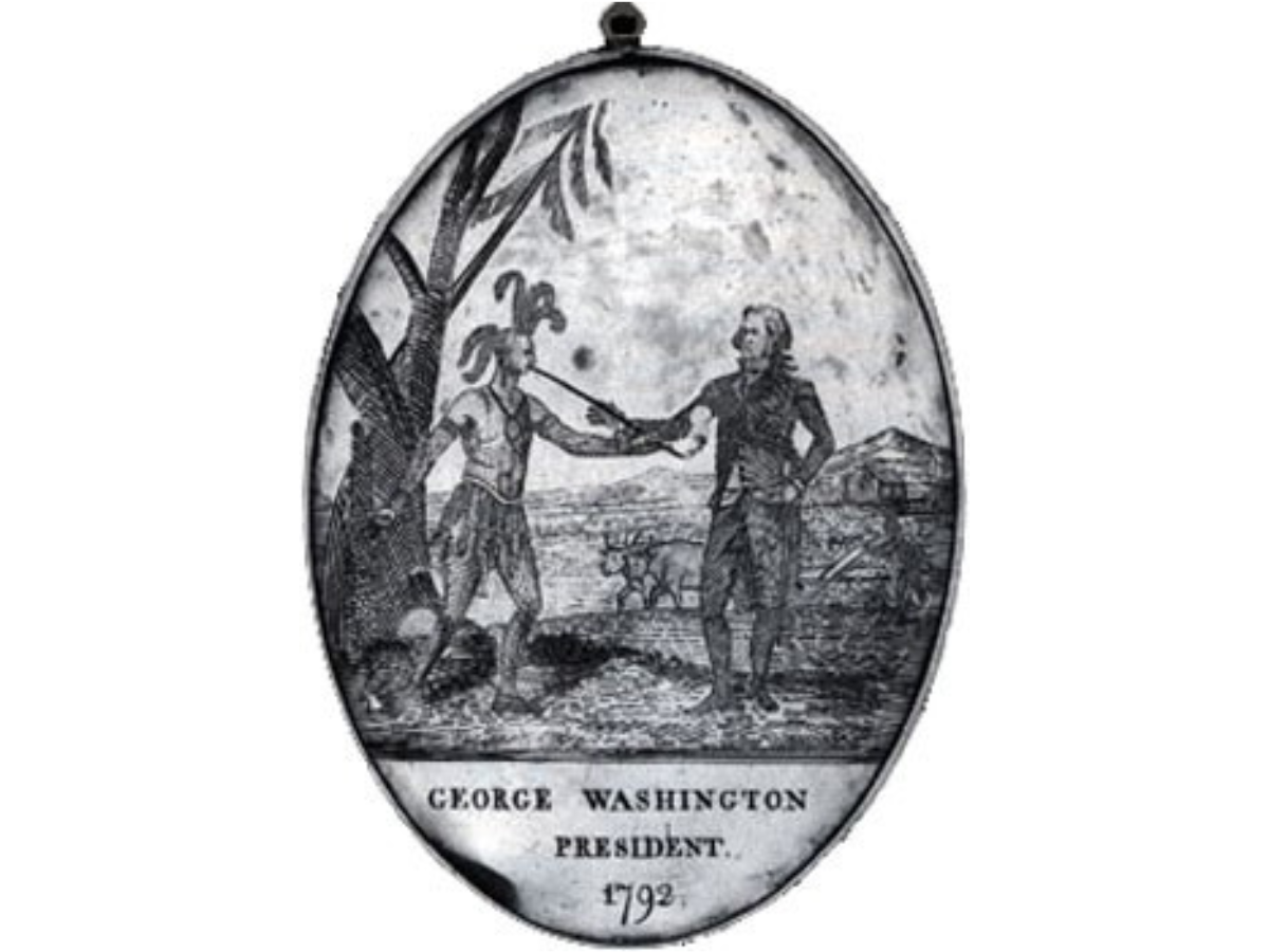 An American peace medal portraying George Washington offering a long pipe to a First Nations Leader. Text at the bottom reads, “Geroge Washington / President / 1792”.