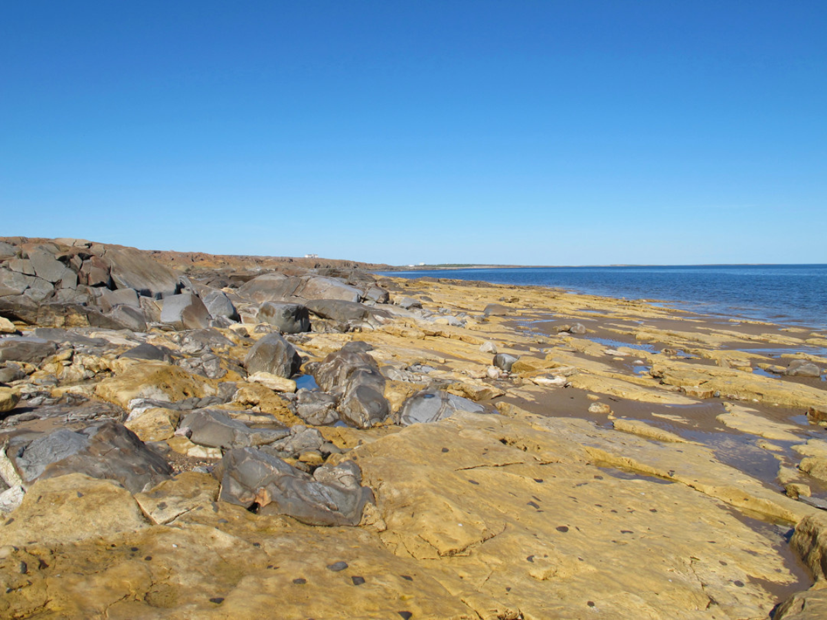 Landscape photo of a rocky shoreline with a incline going up to boulders on the left edge from the waterline on the right edge.