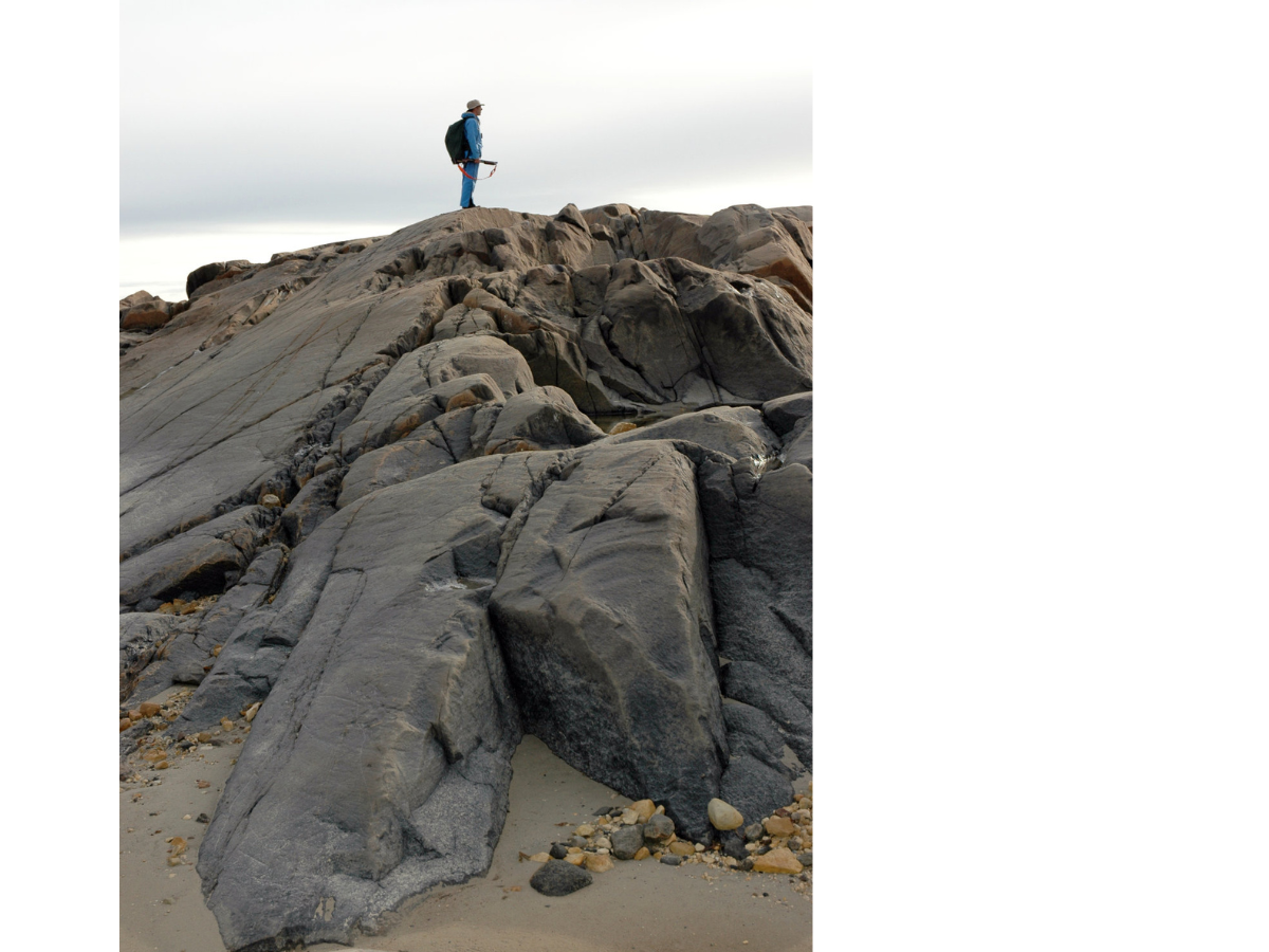 An individual standing at the top of a tall rocky rise from the sand.