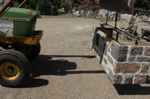 The rectangular base of the frame now with fieldstone blocks attached, being lifted with chains by a tractor.