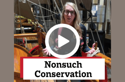 A screenshot of a video, an individual standing on the deck of a wooden ship. There's a play button over the screenshot and overlaid text reads, "Nonsuch Conservation".