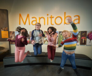 Four smiling children jump up in a fun pose for the picture in the Manitoba Museum Welcome Gallery.