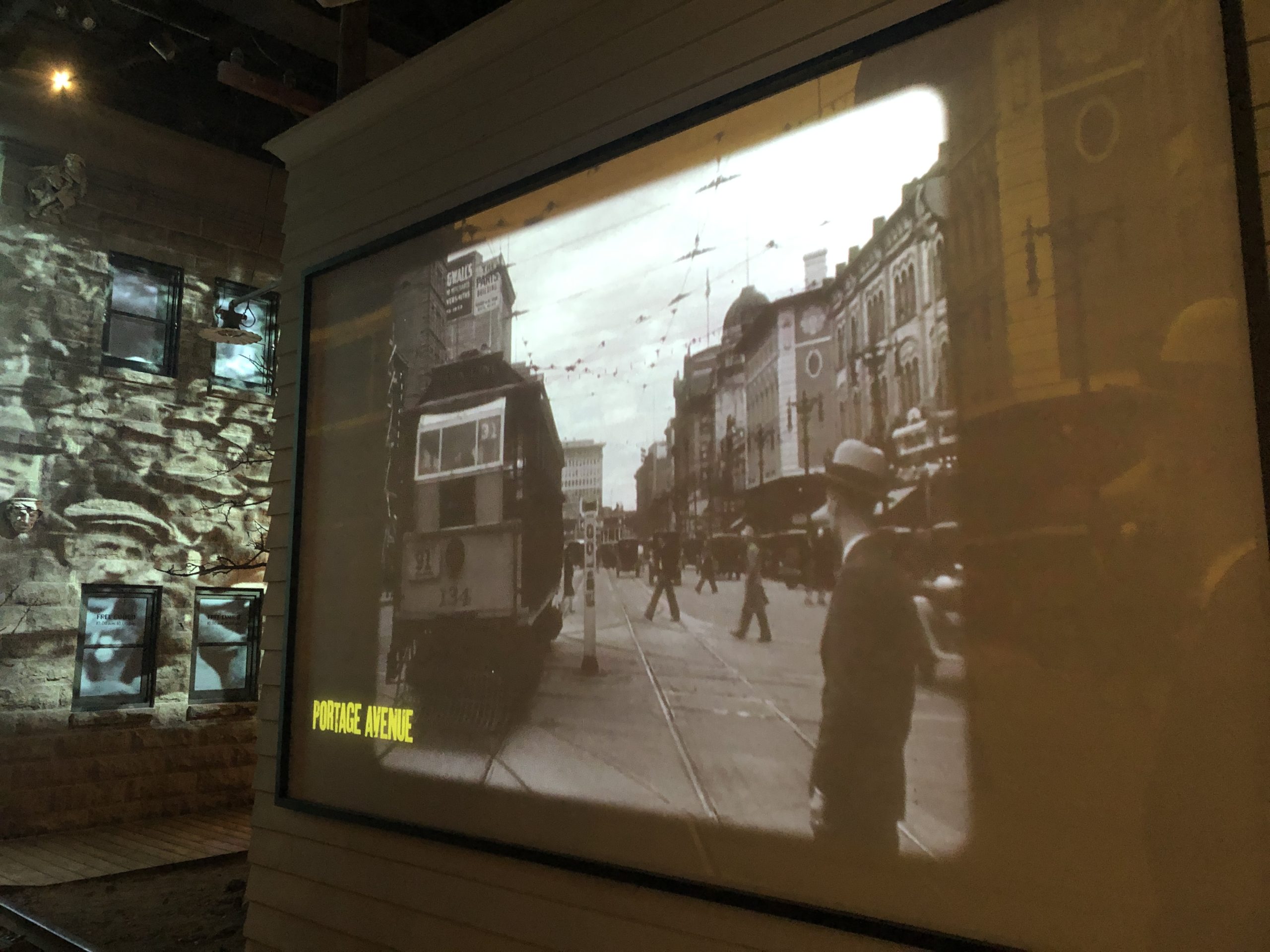 Black and white video footage of traffic on a street in the early 1900s projected onto a faux building exterior. The footage is labelled "Portage Avenue".