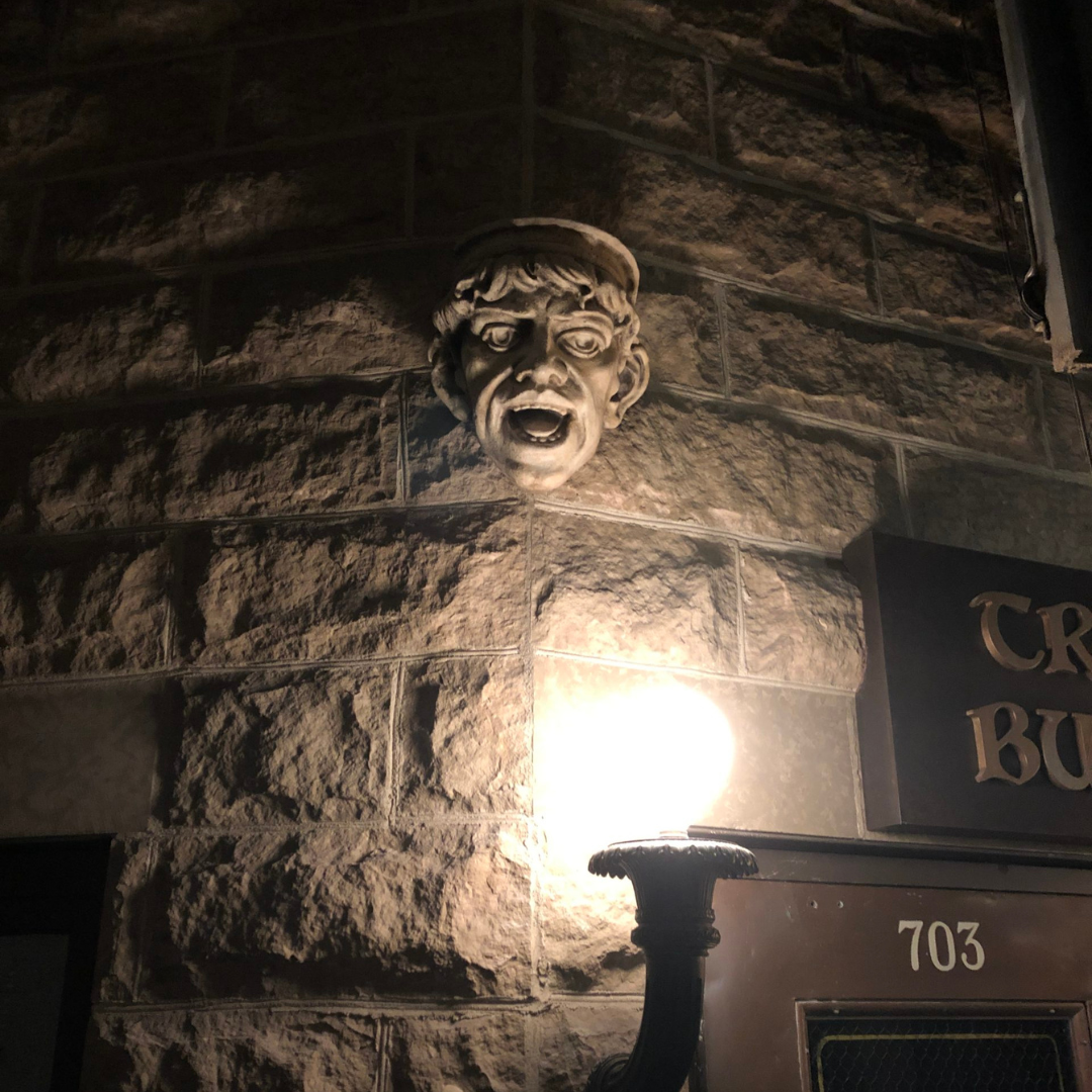 A terracotta grotesque smiling down from a building corner, illuminated by a street light below.