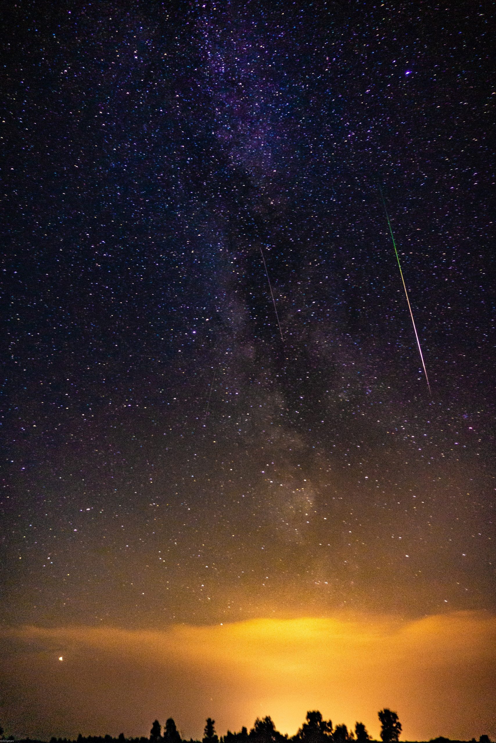 A photograph of several meteors shooting past in the night sky as the last bits of sunset fade away near the horizon.