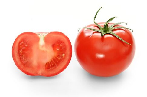 Two red tomatoes on a white background. The tomato on the left is cut open, showing the inside. The tomato on the right is whole.