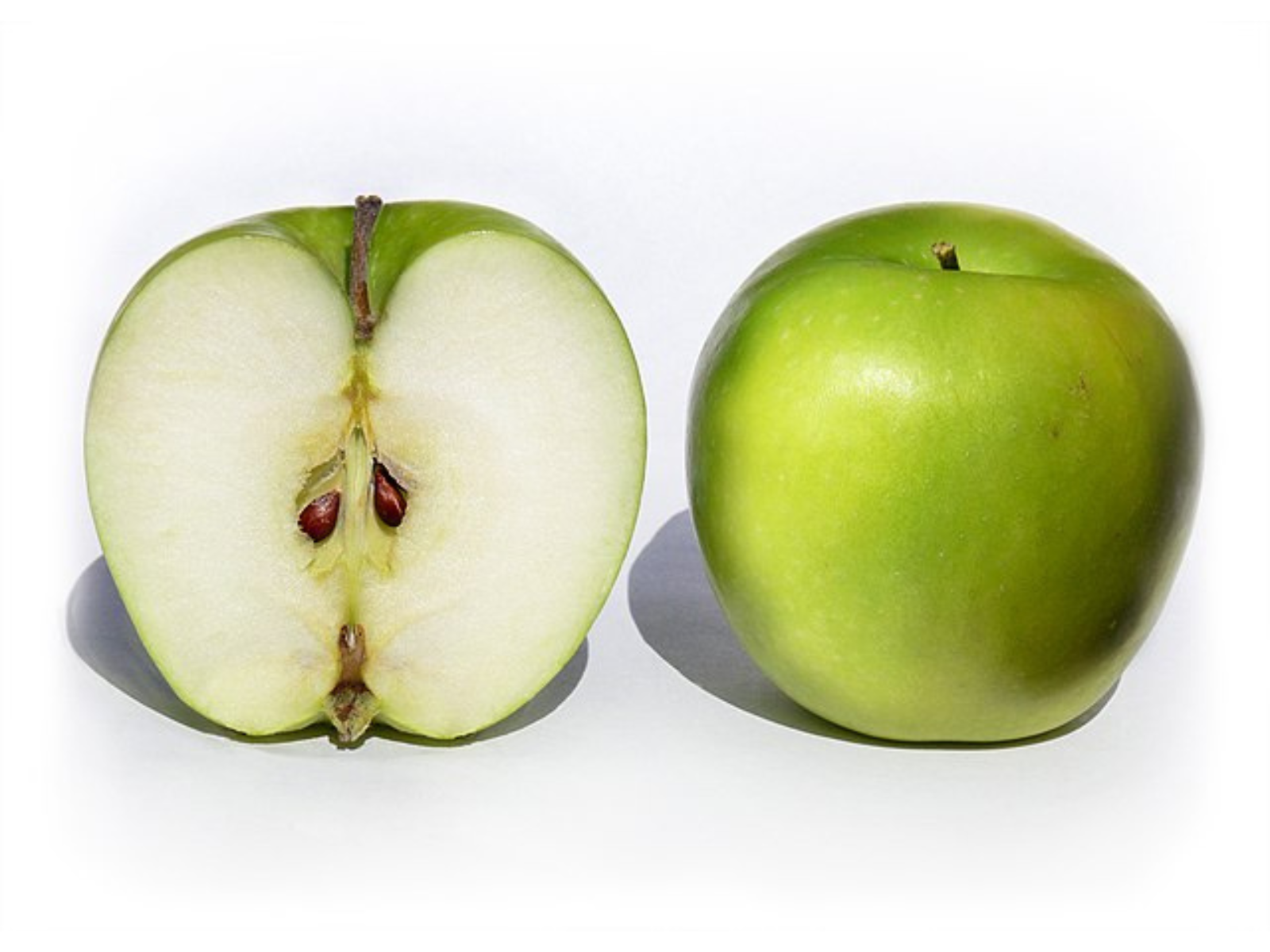 Two apples on a white background. The apple on the left is cut open, showing the inside. The apple on the right is whole showing its green skin.