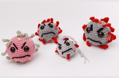 Four crocheted COVID molecules with frowning faces. One ball is pink with grey, and the other three are grey with red.