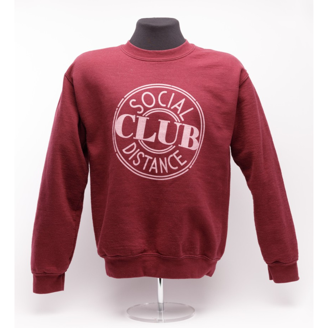 A red sweatshirt on a mannequin bust. The from of the sweater reads, "Social Distance Club".