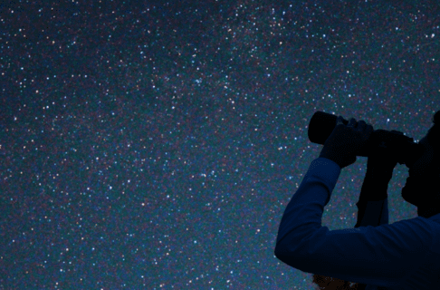 A man looks at the sky with binoculars.